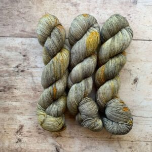 Three skeins of Merino Flax in Feather, a grey, cream, yellow and orange speckled yarn