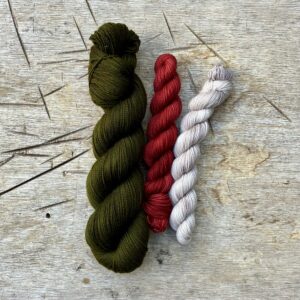 A full skein of sock wool in a deep, rich moss green with two smaller skeins, one red the other stone coloured