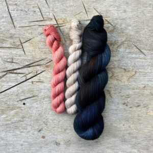A full skein of sock wool in a dark blue green with two smaller skeins, one pink the other creamy buff coloured