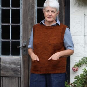 A woman standing in front of a glazed door wearing a sleeveless vest in a russet brown